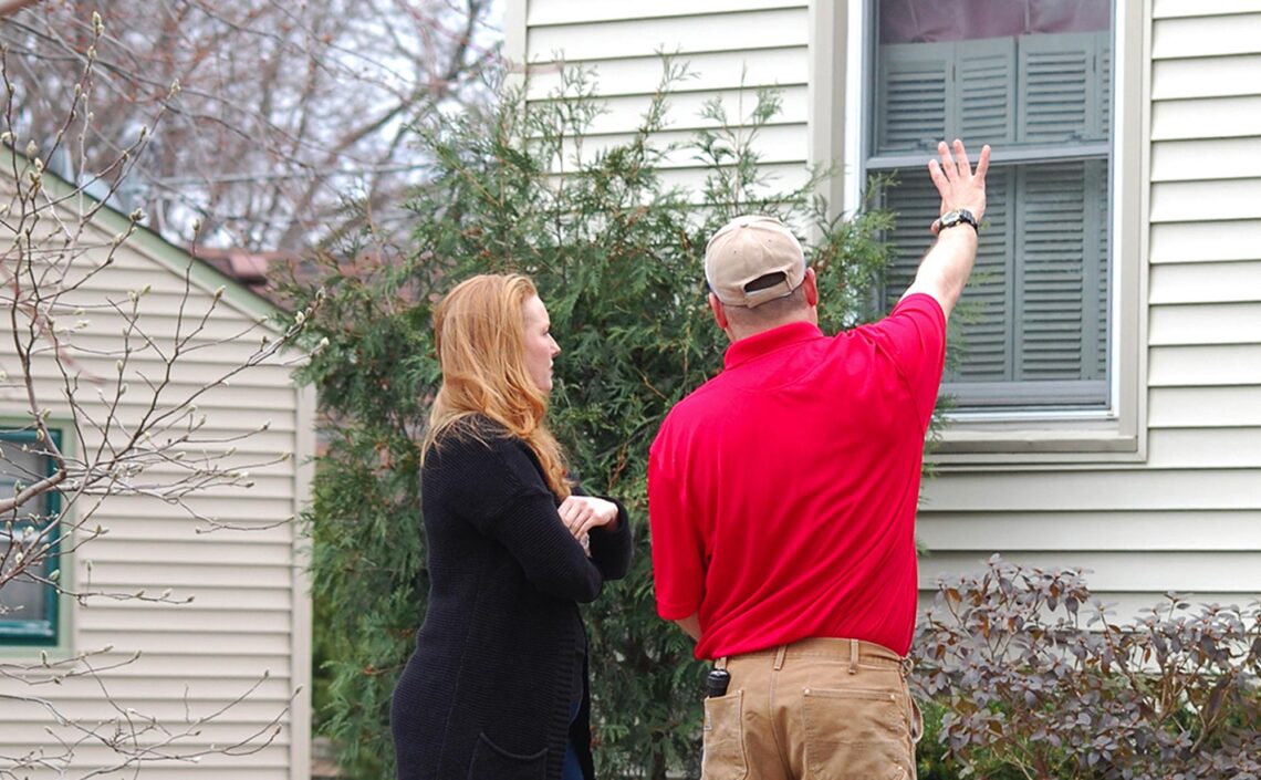pest control technician pointing to home with homeowner in front yard