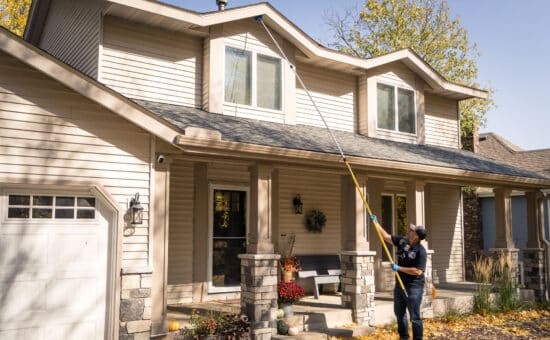 A pest technician clearing a wasp nest from the second story of a house