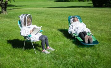 two kids wearing bee suits to avoid being bitten by mosquitoes while sitting in lawn chairs outside